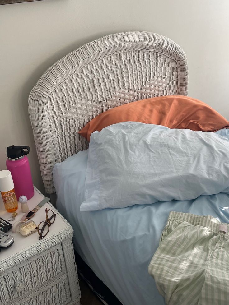 an unmade bed with blue sheets, orange pillows and a cell phone on it