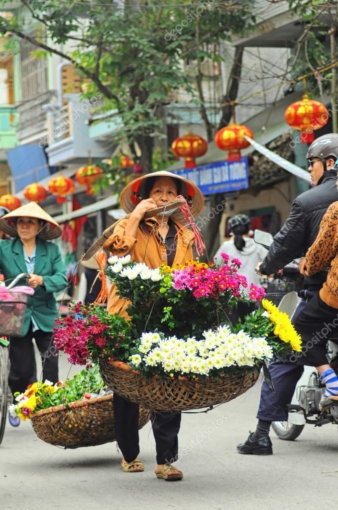 people walking down the street with baskets full of flowers on their backs and one person riding a bike