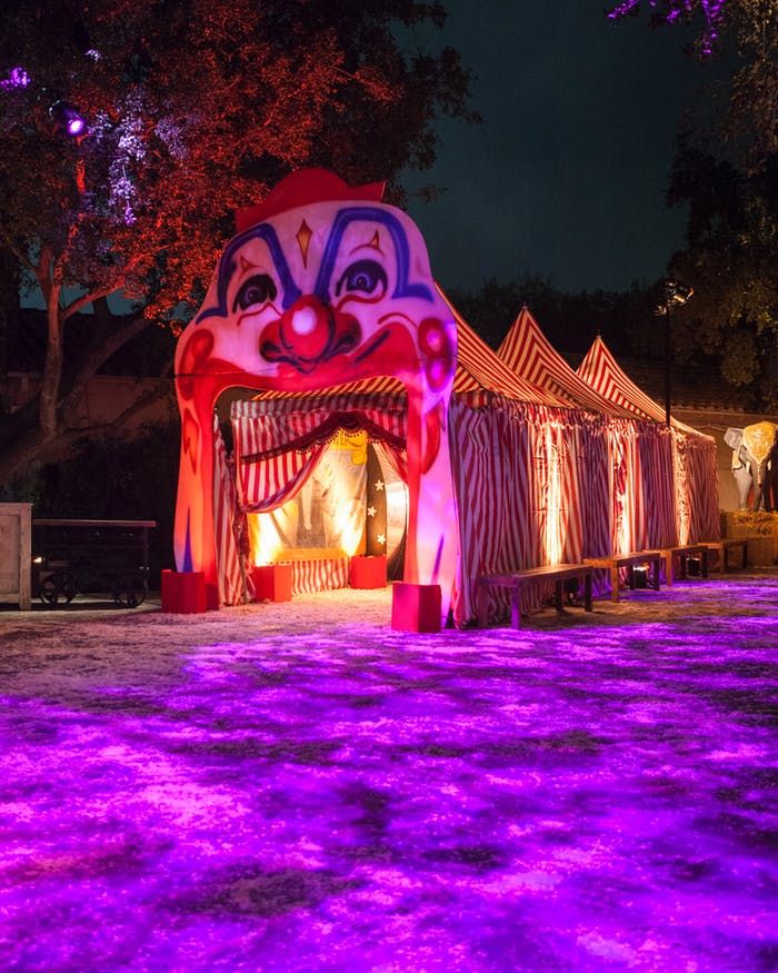 a circus tent lit up at night with purple lights on the ground and decorations around it