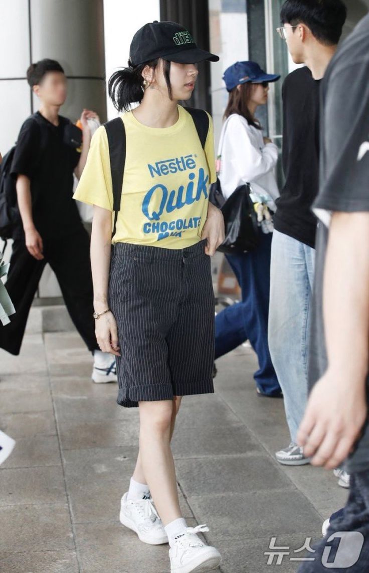 a woman in a yellow shirt and black skirt is walking down the street with other people