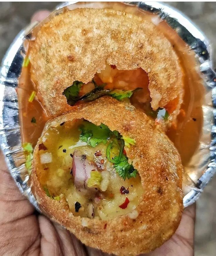 a hand holding a half eaten food item in foil wrapper with broccoli and cheese inside