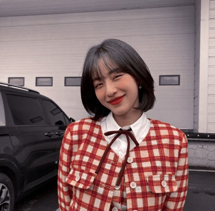 a woman wearing a red and white checkered jacket standing next to a black suv