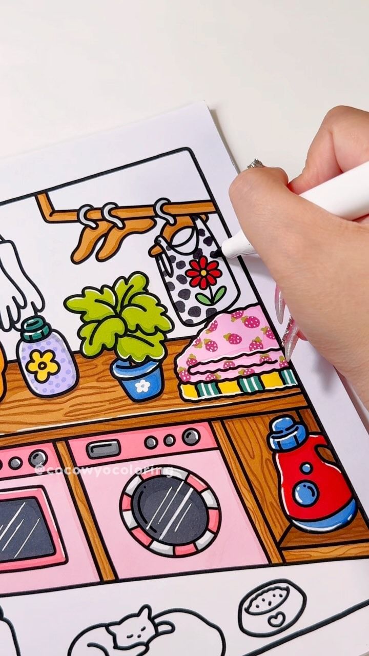 a person is holding a marker over a coloring book with an image of a kitchen