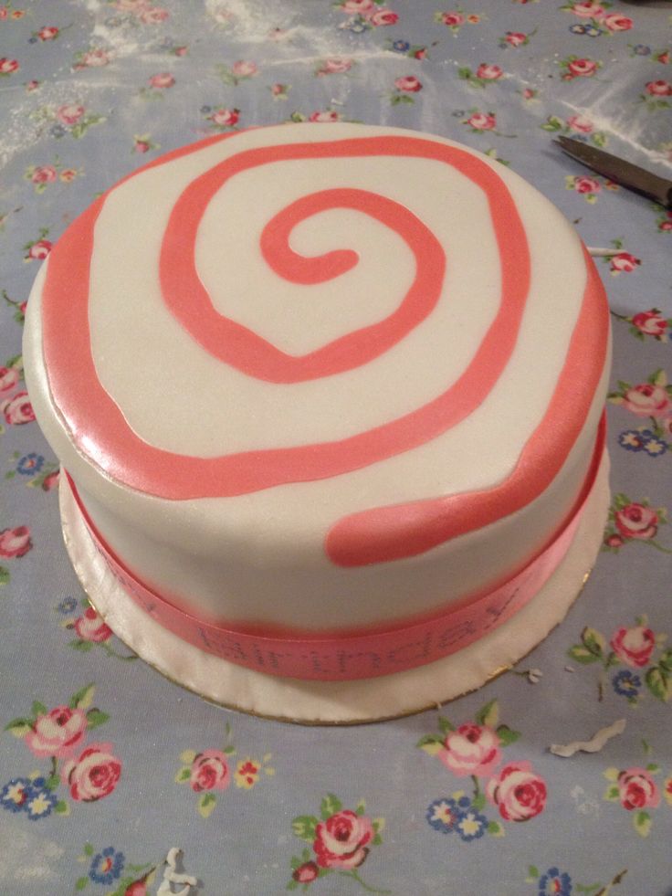 a white and red cake with pink swirls on it sitting on a floral table cloth