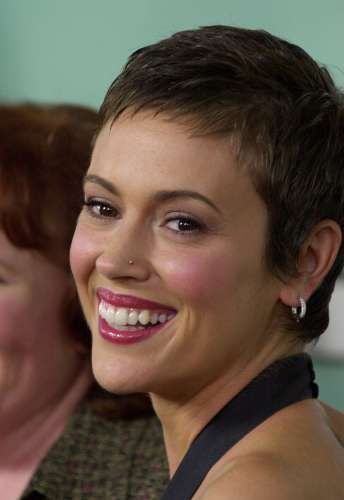 a woman with short hair smiling at the camera and another person in the background behind her