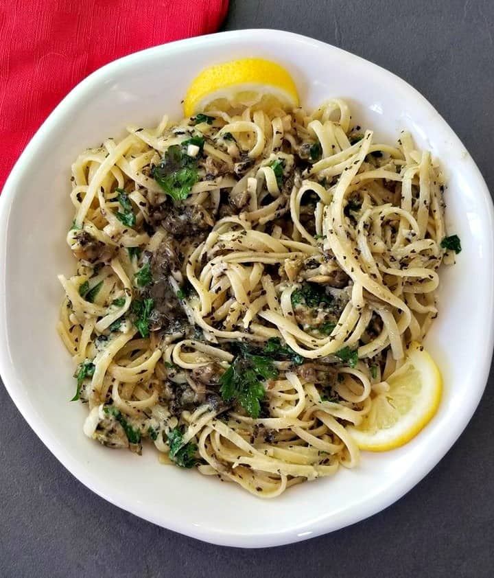 a white bowl filled with pasta and meat next to a lemon wedge on top of a table