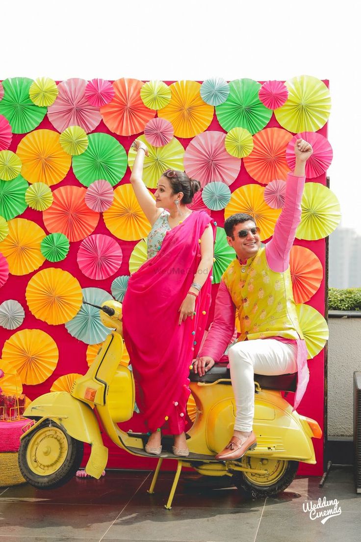 two people sitting on a scooter in front of a wall with umbrellas