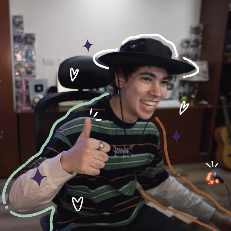 a young man wearing a hat and giving the thumbs up sign while sitting in an office