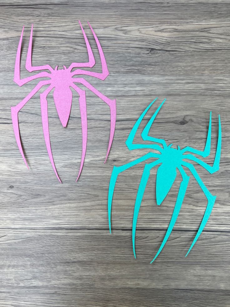 two spider - man paper cut outs sitting on top of a wooden table