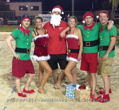 a group of people dressed up as santa clause on the beach at christmas time with gifts in front of them