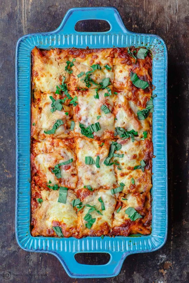 a blue casserole dish filled with lasagna sauce and fresh basil leaves