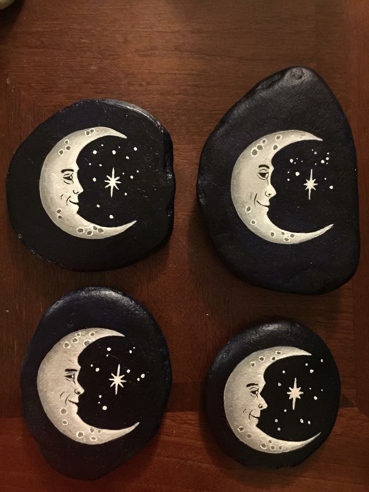 four painted rocks with the moon and stars on them, sitting on a wooden table