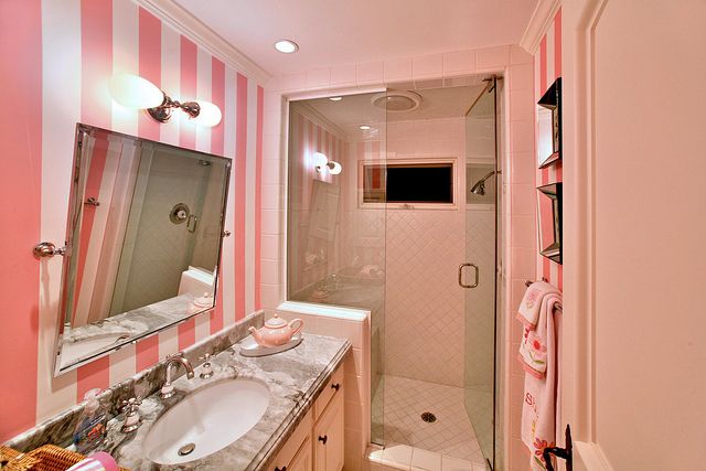 a bathroom with pink and white stripes on the walls, two sinks and a walk in shower