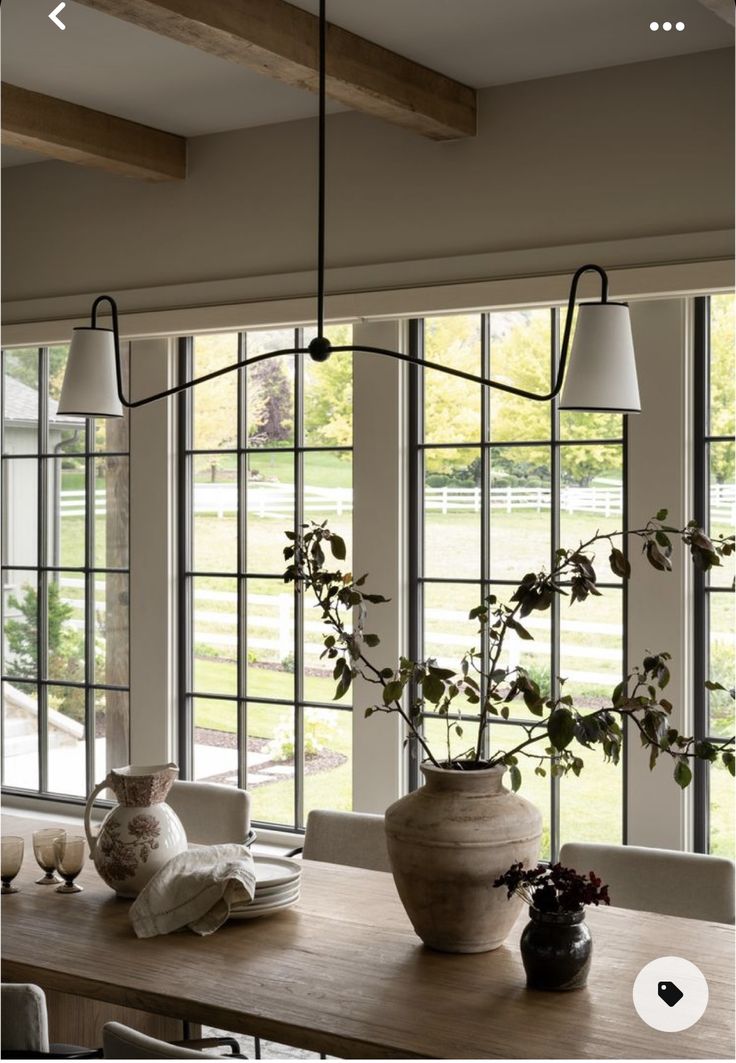 a dining room table with vases and plants on it in front of large windows