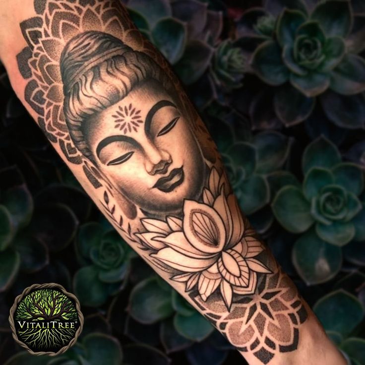 a person with a tattoo on their arm that has a buddha face and flowers around it