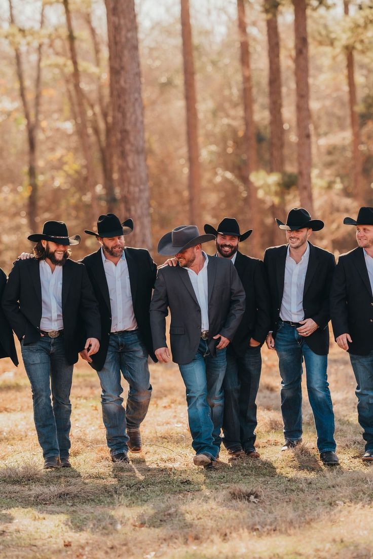 a group of men in cowboy hats are walking through the woods with their backs to each other