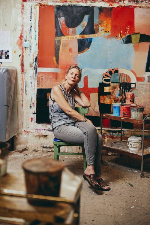 a woman sitting on a chair in front of a wall with art work behind her