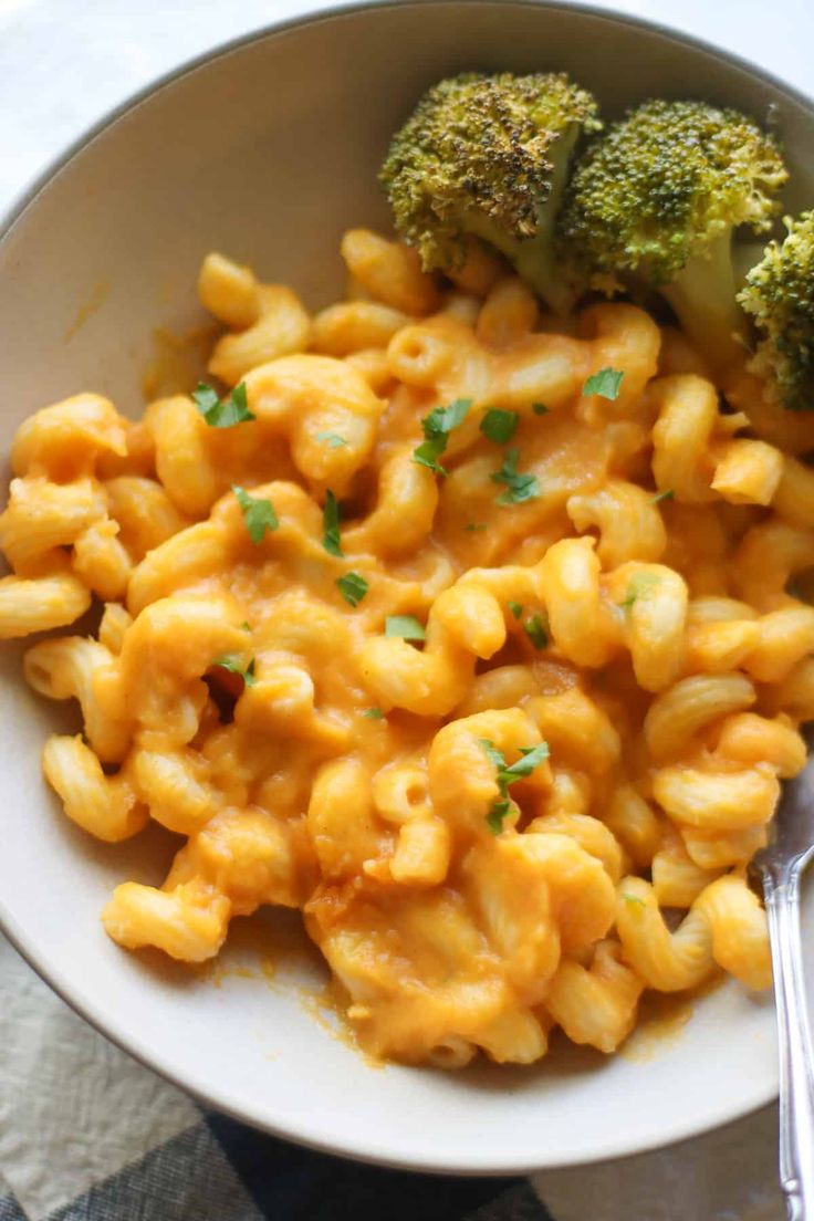 a white bowl filled with macaroni and cheese next to broccoli on a table