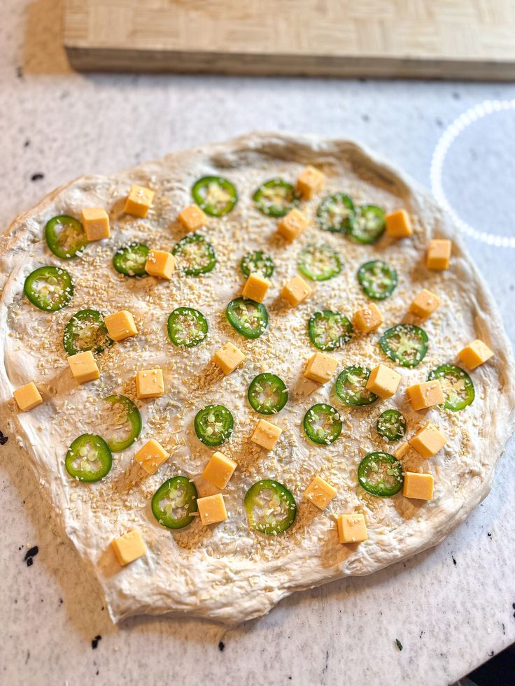 an uncooked pizza with cheese and jalapenos on it sitting on a counter