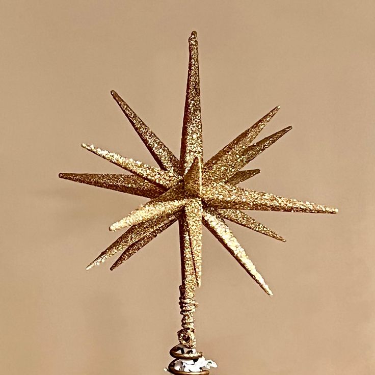 a gold star ornament hanging from a hook on a brown wall in front of a tan background