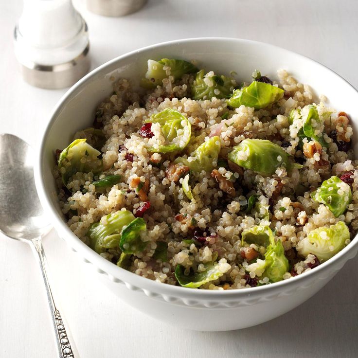 a white bowl filled with rice and vegetables next to a silver spoon on top of a table