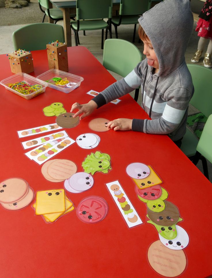 a young boy sitting at a table with paper cut out of food on top of it