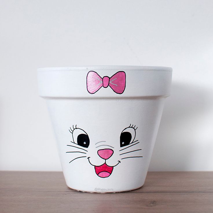 a white flower pot with a cat face painted on the front and pink bow tie