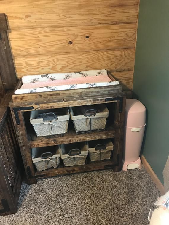 a baby crib with baskets on the bottom shelf next to a pink trash can