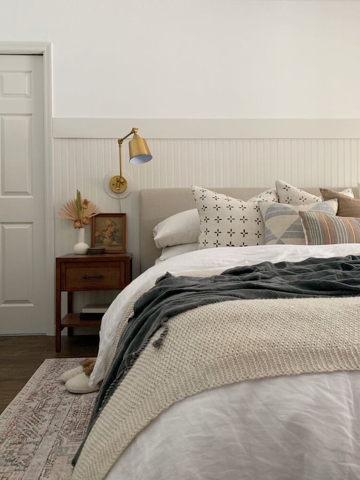 a bed with pillows and blankets on top of it next to a lamp in a room