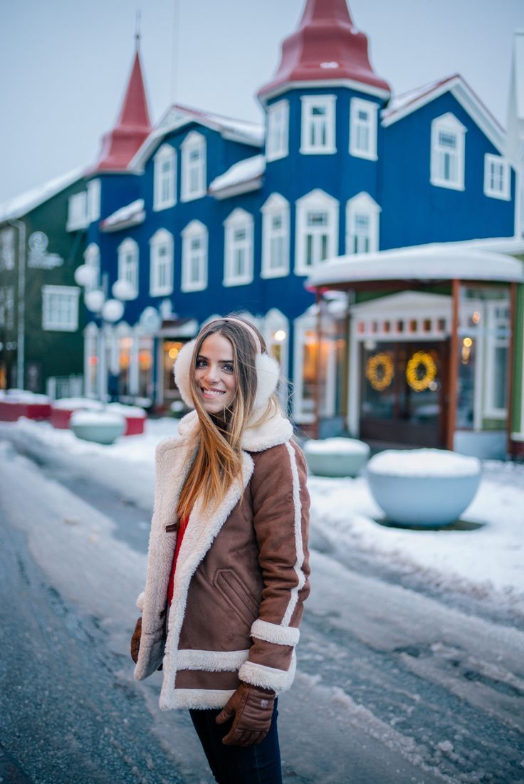 a woman standing in front of a blue building with snow on the ground and buildings behind her