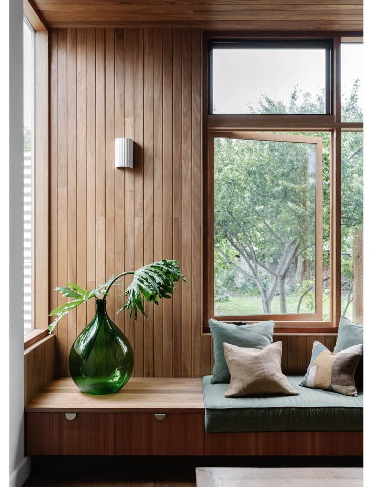 a green vase sitting on top of a window sill next to a wooden bench