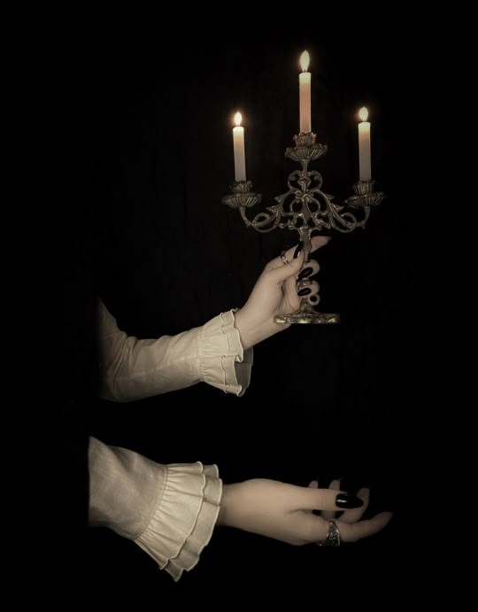 a woman holding a candle in her hand with two candles on the wall behind her