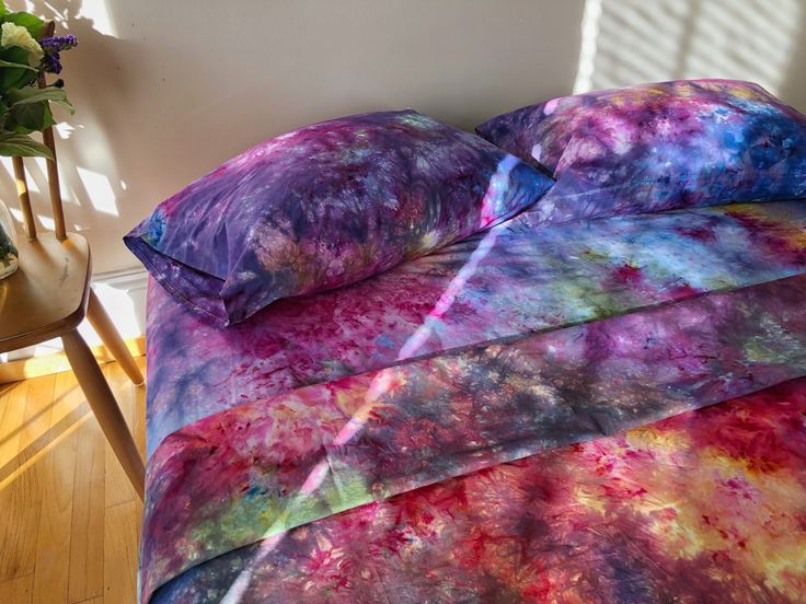 a bed covered in a purple and blue comforter next to a vase with flowers