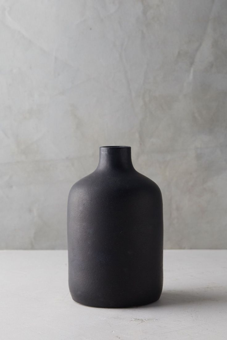 a black vase sitting on top of a white table next to a gray wall and floor