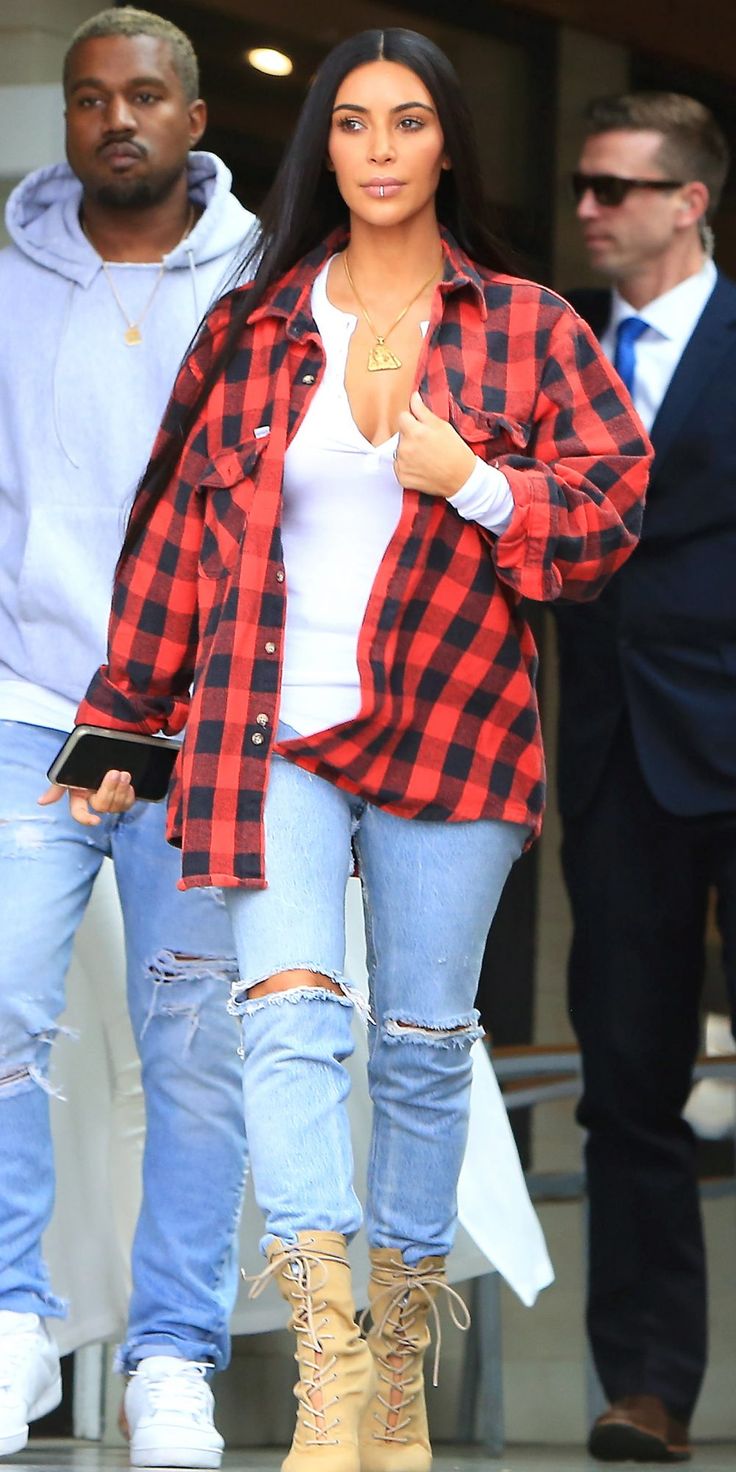 a woman in ripped jeans and plaid shirt is walking down the street with her hand on her hip