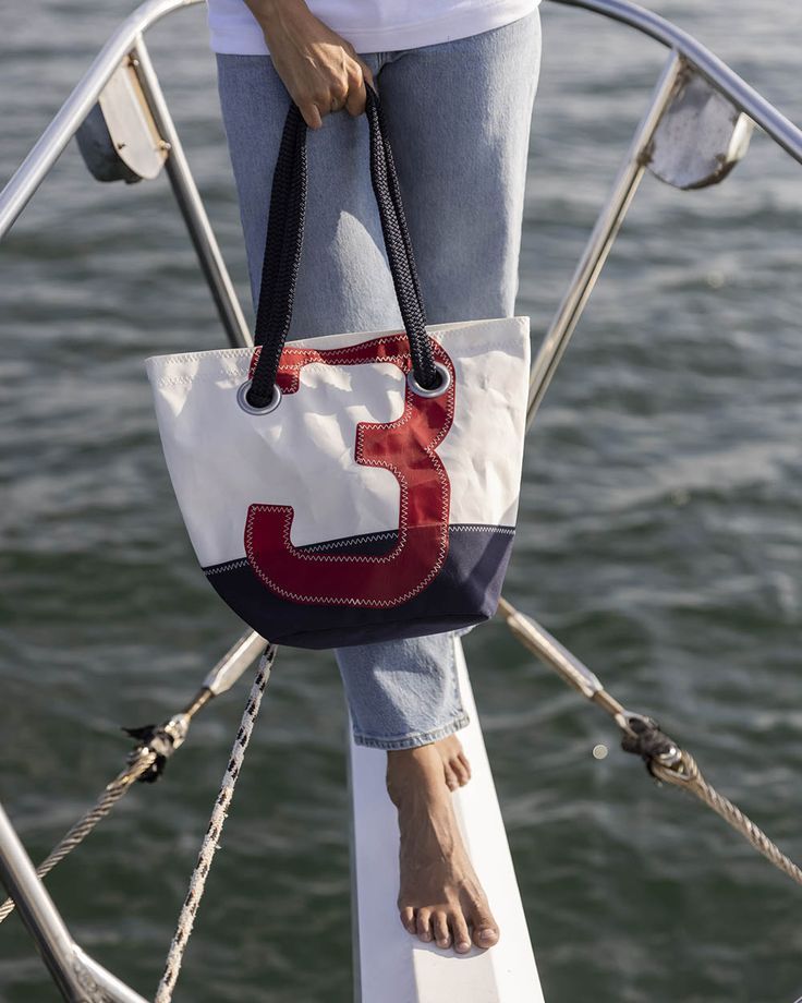 The Legend Handbag from our Navy collection is made of a navy fabric base, 100% white recycled sailcloth and a large red “3”, sewn with our iconic zigzag stitch. An authentication card is sewn inside and certifies the origin of the sail. Everyday Rectangular Light Grey Bag, White Nautical Bag For Everyday, Nautical Style Navy Bag For Everyday Use, Sail Colored Rectangular Travel Bag, Nautical Navy Bag For Everyday Use, Navy Summer Tote Beach Bag, Nautical Style Sail Color Bags For Daily Use, Everyday Nautical White Bag, Travel Canvas Bag In Sail Color