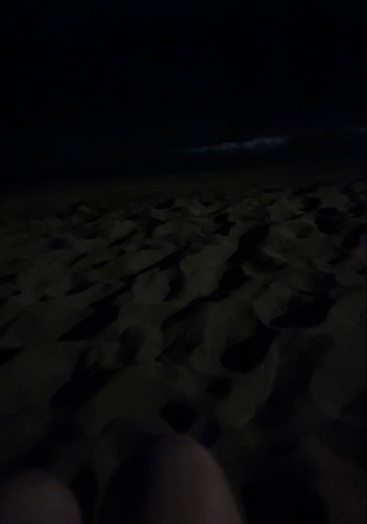 someone is sitting on the beach at night with their feet in the sand and there are no people around