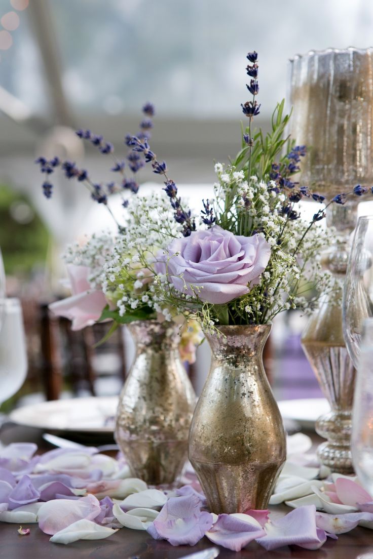 purple flowers are in vases on a table with silver plates and wineglasses