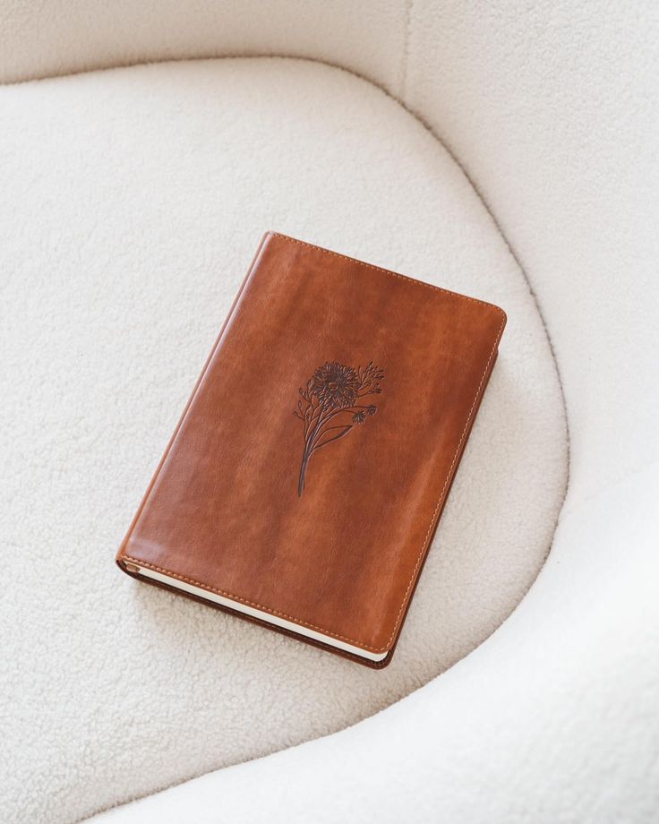 a brown leather book sitting on top of a white chair next to a plant pot