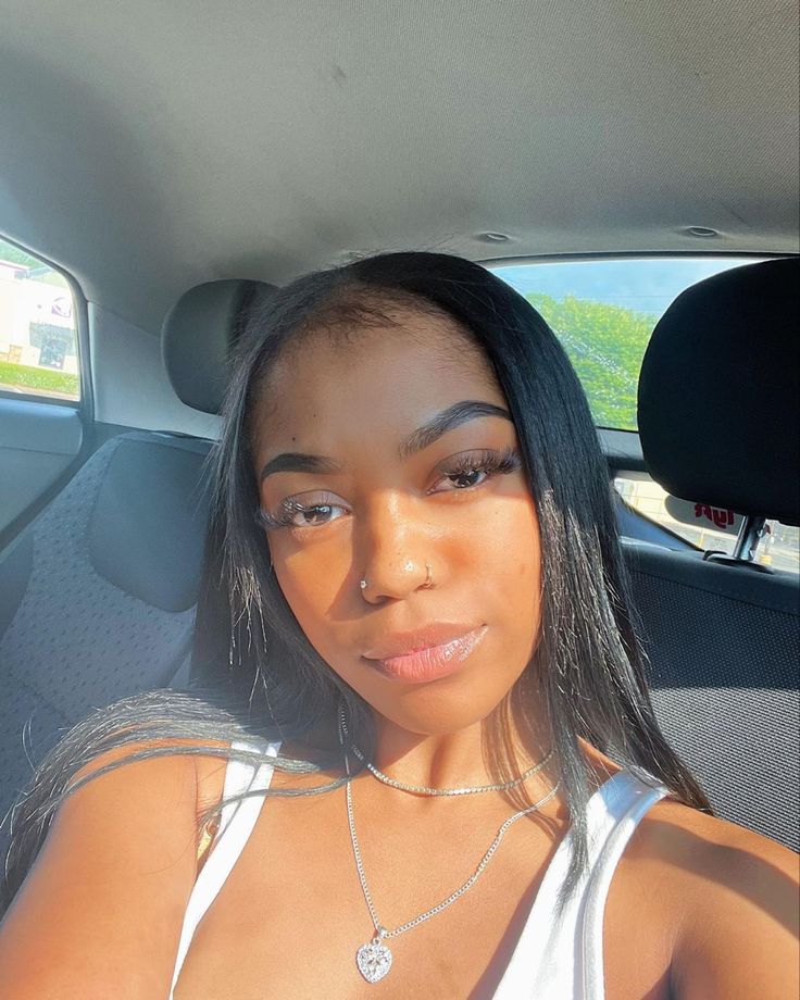 a woman sitting in the back seat of a car wearing a white tank top and silver necklace