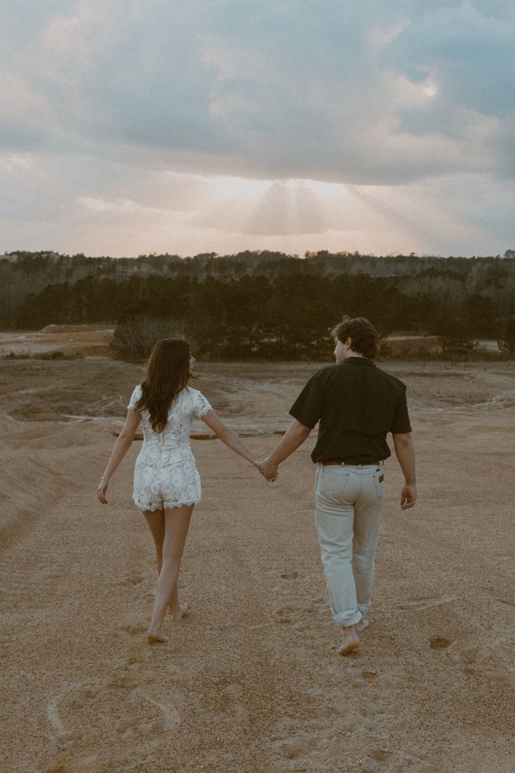 a man and woman holding hands while walking through the desert at sunset or sunrise with sunbeams in the sky