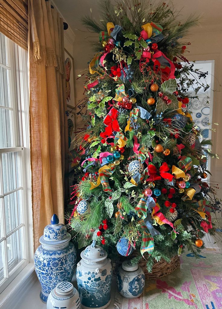 a decorated christmas tree in the corner of a room with blue and white vases