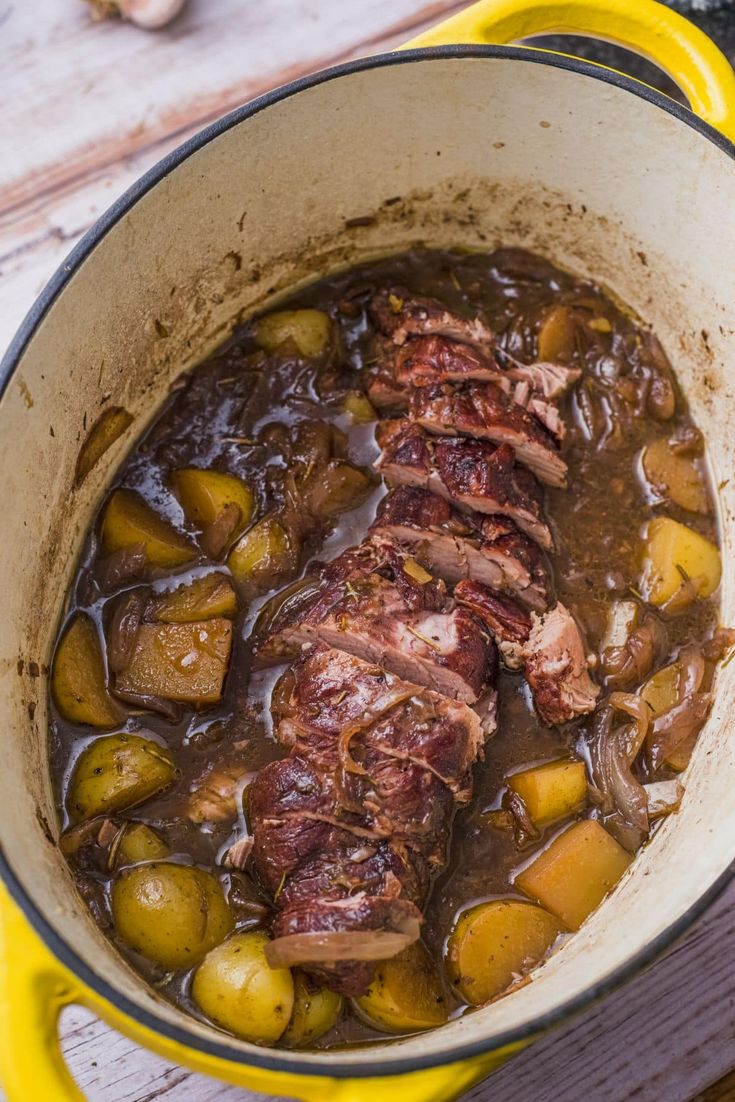 a pot filled with meat and potatoes on top of a wooden table