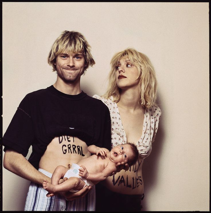 a man holding a baby while standing next to a woman with tattoos on her stomach