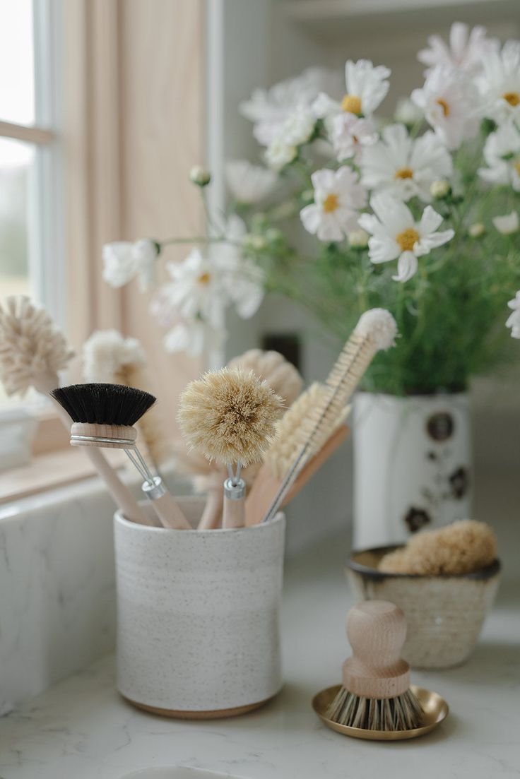 some brushes are sitting in a cup on a counter next to a vase with white flowers