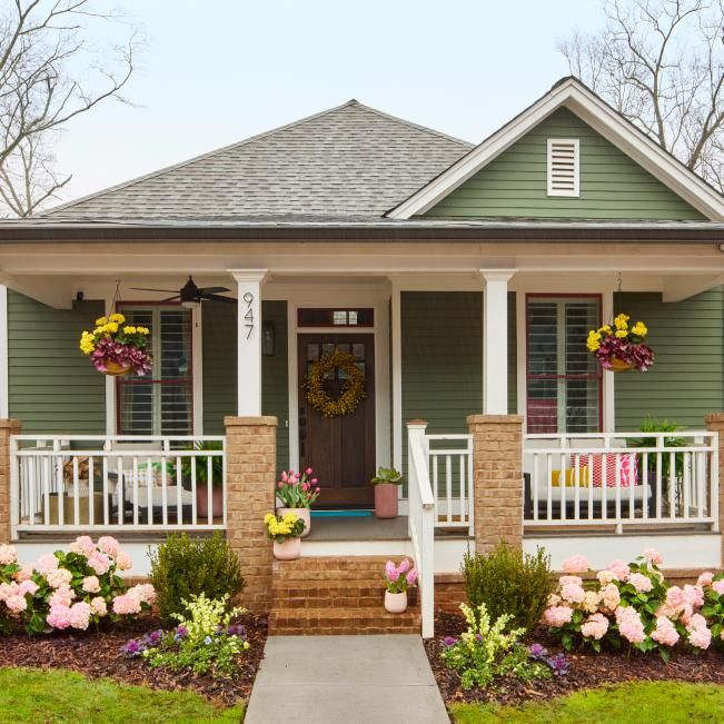 a small green house with flowers and wreaths on the front porch, along with steps leading up to the front door