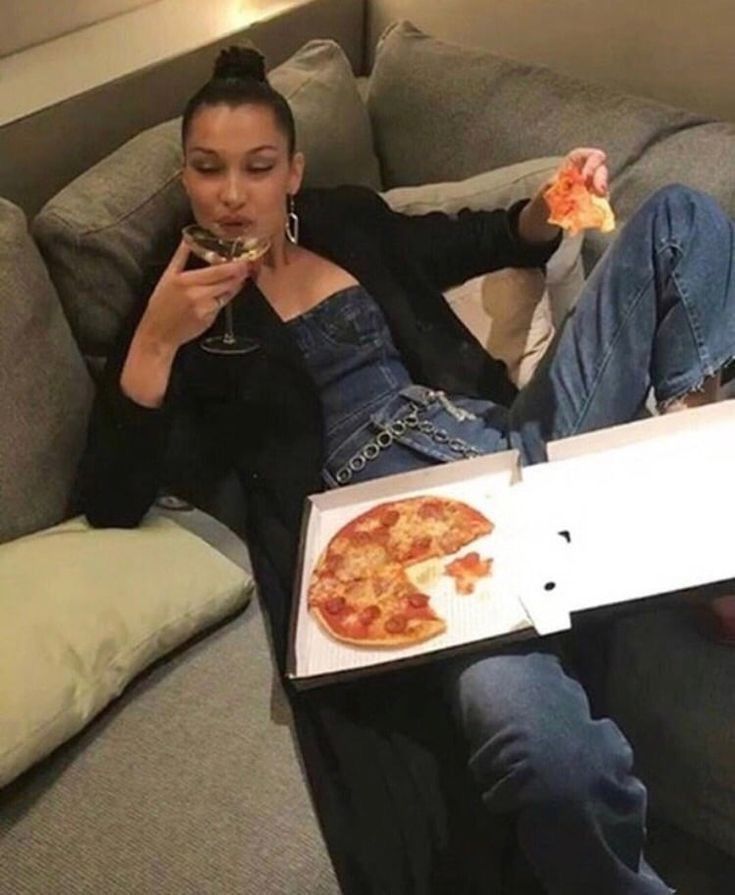 a woman sitting on a couch eating pizza and drinking wine