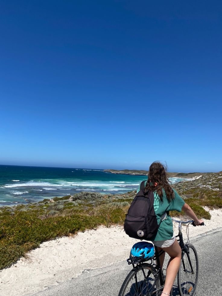 a woman riding a bike down a road next to the ocean