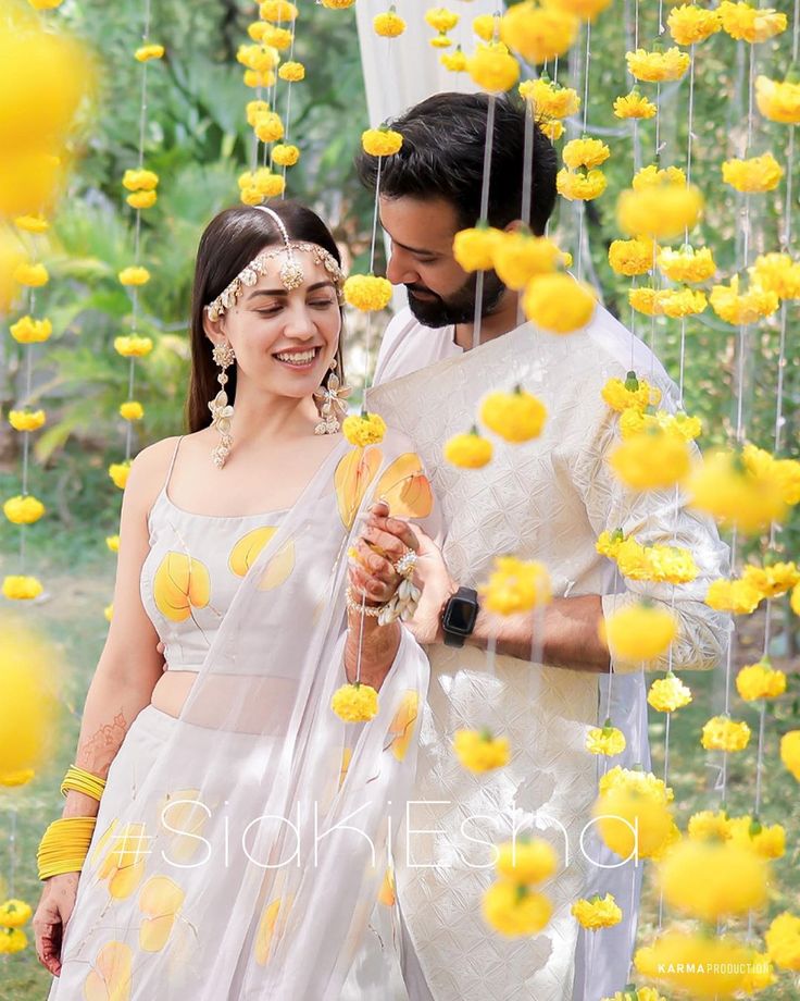 a man and woman standing next to each other in front of yellow flowers