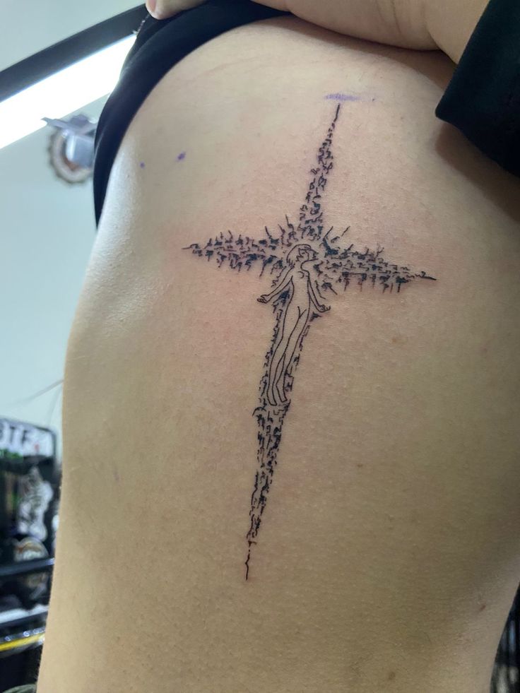 a cross tattoo on the back of a woman's lower back ribcage